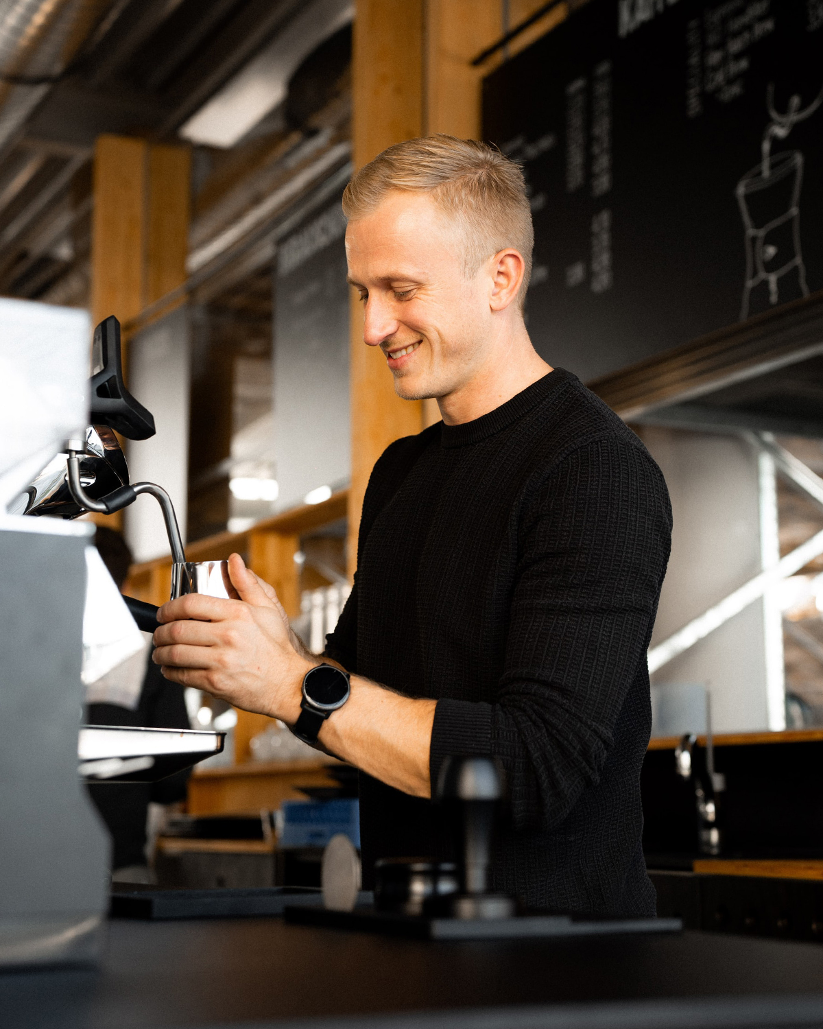 Christoph Klescher, der Geschäftsführer von Paul & Bohne, steht vor einer Kaffeemaschine und schäumt Milch auf.