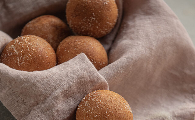Viele Jako-Mini Bällchen liegen mit Zimt und Kristallzucker bestreut auf einem rosa Leinentuch.