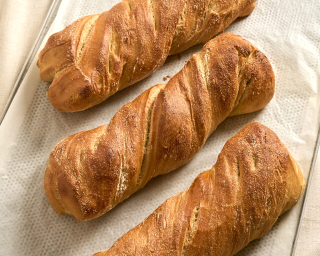 Drei helle längliche Pane Rustico liegen auf beigem Untergrund.