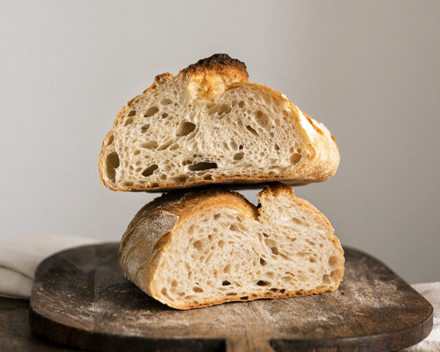 Toskanabrot liegt auf einem Holzbrett. Das Brot ist angeschnitten und man sieht die Schnittfläche des Brotes und die charakteristischen Blasen des Sauerteigs.