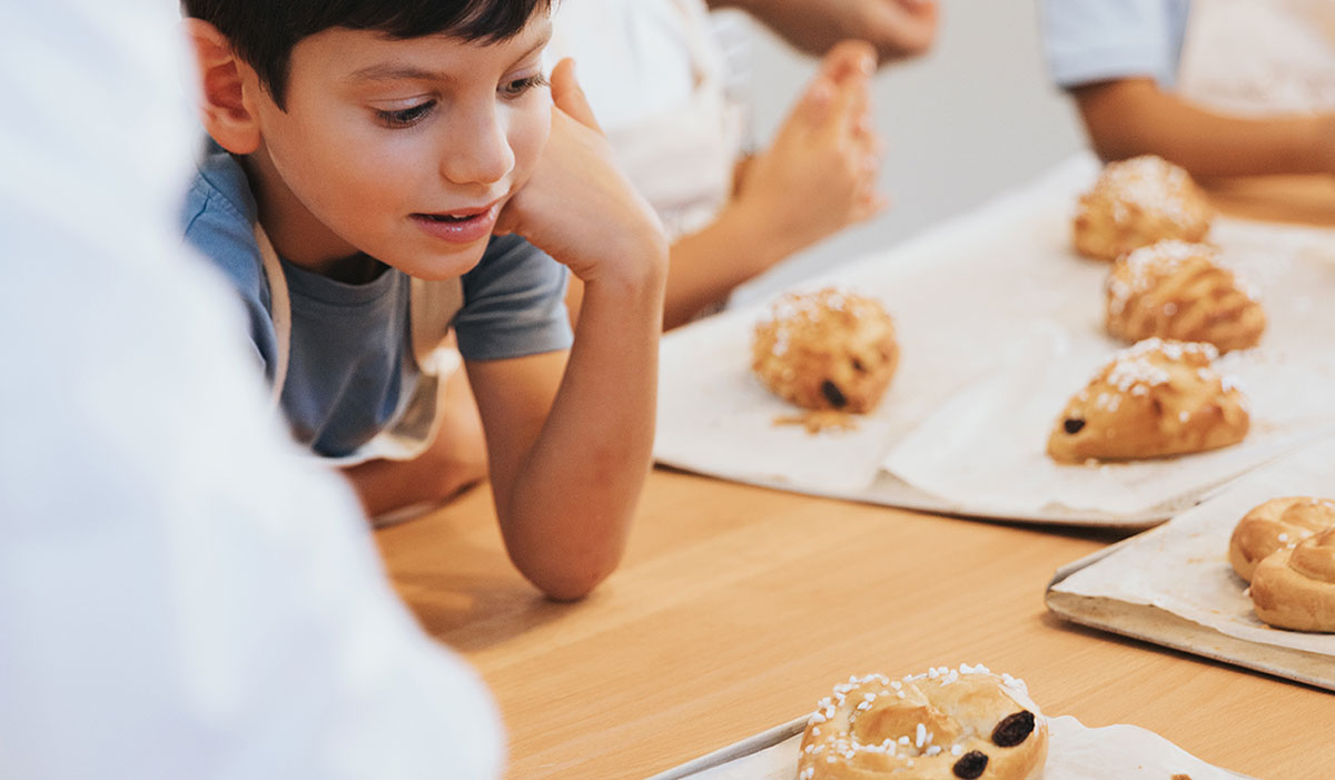 Eine Szene aus einem Kinderbackkurs: Ein Kind schaut sich selbstgebackene Weckerl.