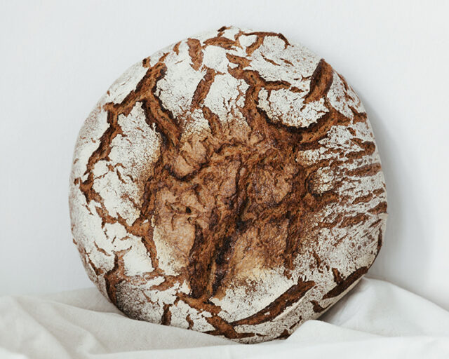 Der große Laib Brot lehnt an der Wand, aufgestellt auf einem hellgrauen Tuch.