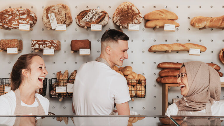Drei Mitarbeiter der Bäckerei Sorger stehen hinter der Theke und lachen.
