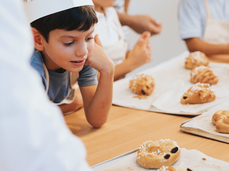 Eine Szene aus einem Kinderbackkurs: Ein Kind schaut sich selbstgebackene Weckerl.