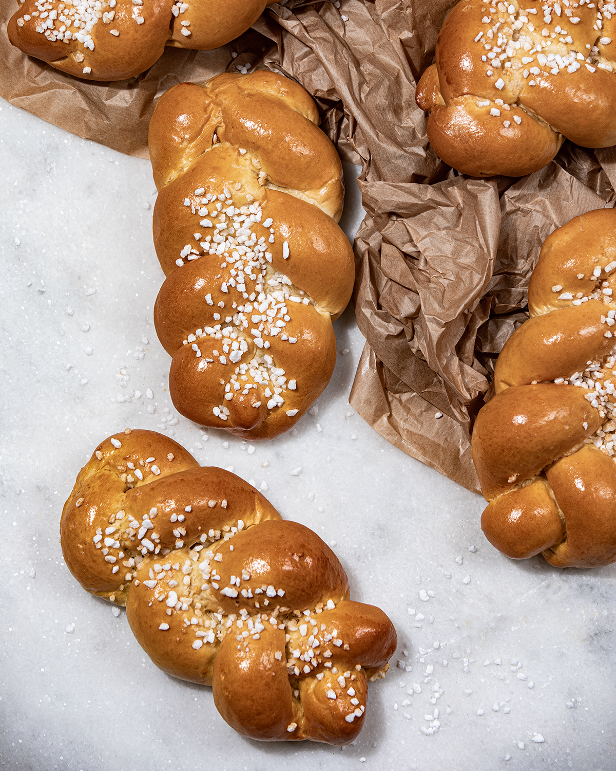 Fünf kleine Striezel, die mit Hagelzucker bestreut sind, liegen auf einer Steinplatte.