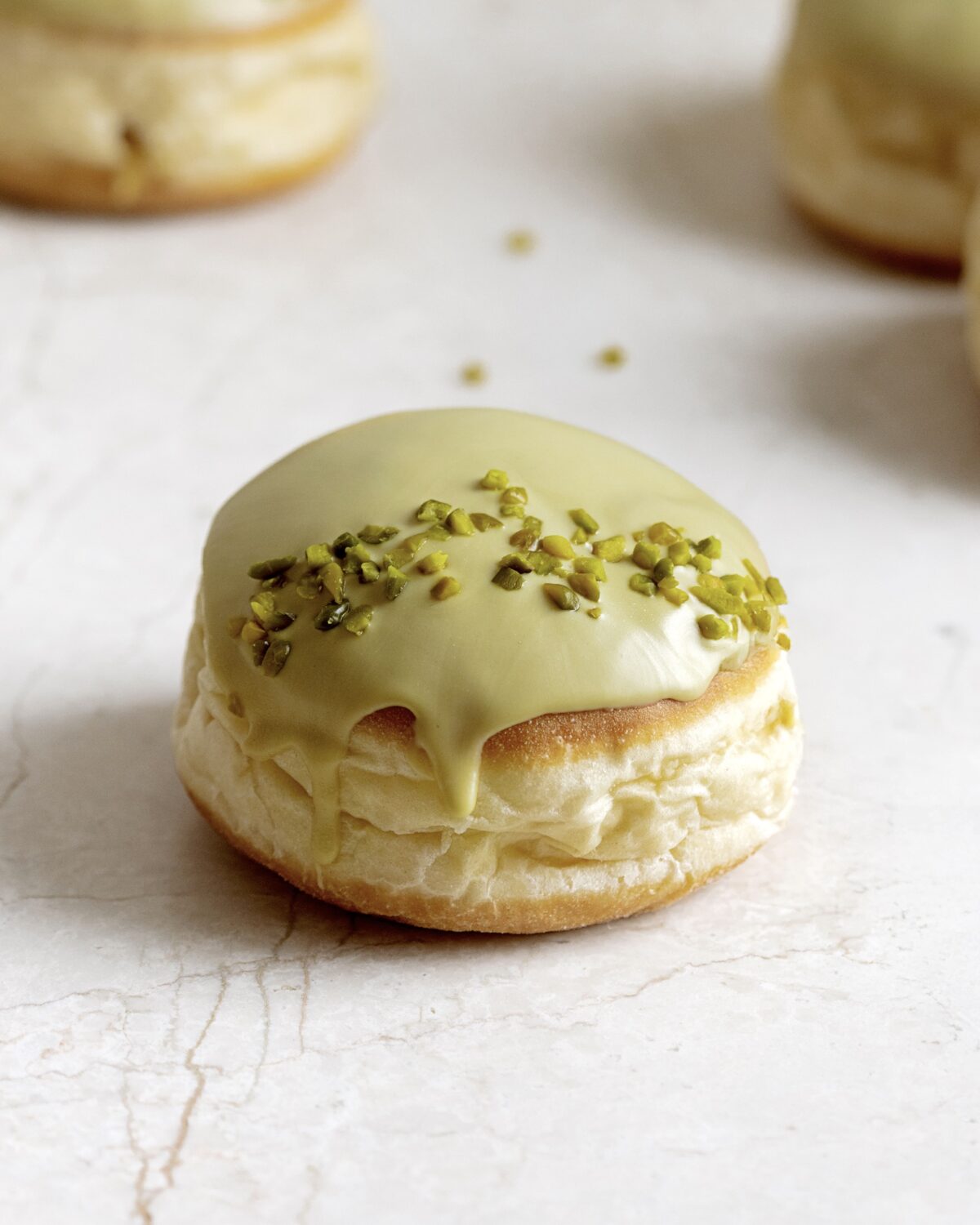 Ein Krapfen mit grüner Glasur und gehackten Pistazien liegt auf einer Steinplatte.