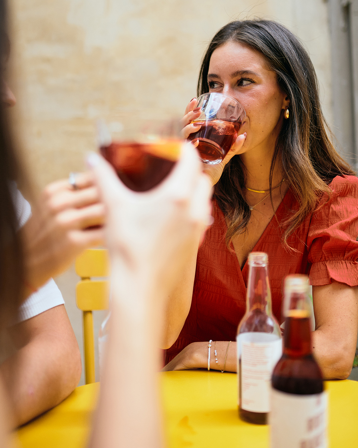 Frau sitzt an gelbem Tisch, auf dem Rote Rakete Falschen stehen. Sie trinkt aus einem Glas.