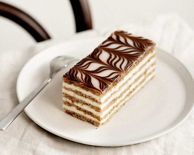 Ein Stück Esterhazy Schnitte auf einem weißen Teller steht auf einem Tisch mit weißem Tischtuch